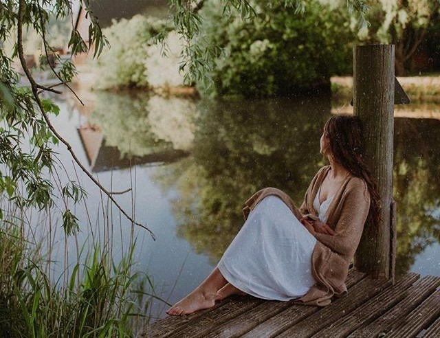 Mujer sentada junto a un lago bajo un sauce, en calma